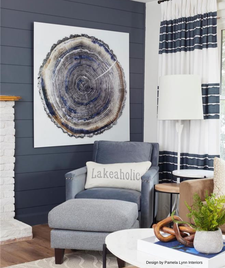 A cozy living room with blue accent wall, tree ring art, and a blue chaise lounge with a lake-themed pillow.