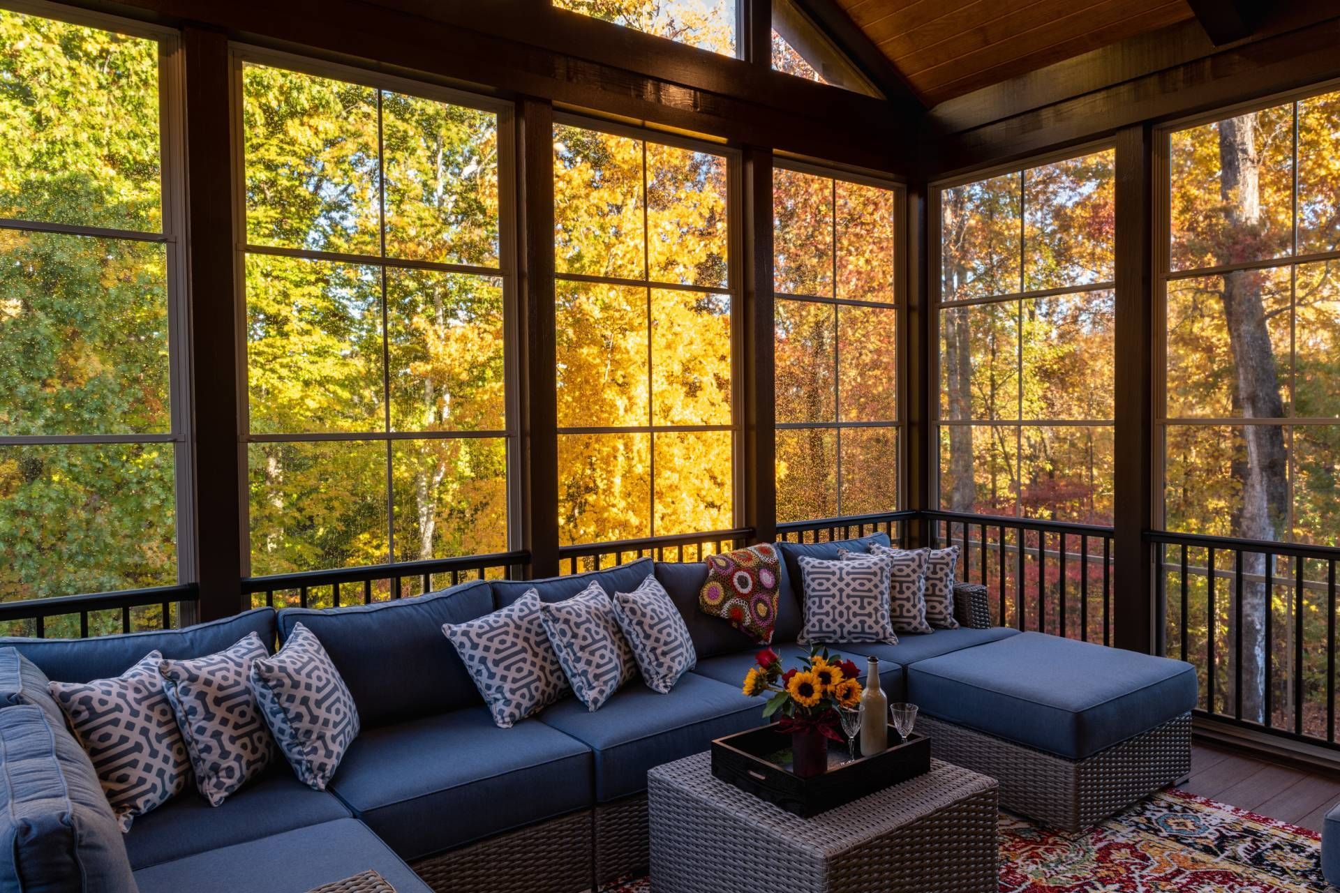 A cosy screened-in porch with jewel-toned outdoor cushions and a stunning fall view from the windows