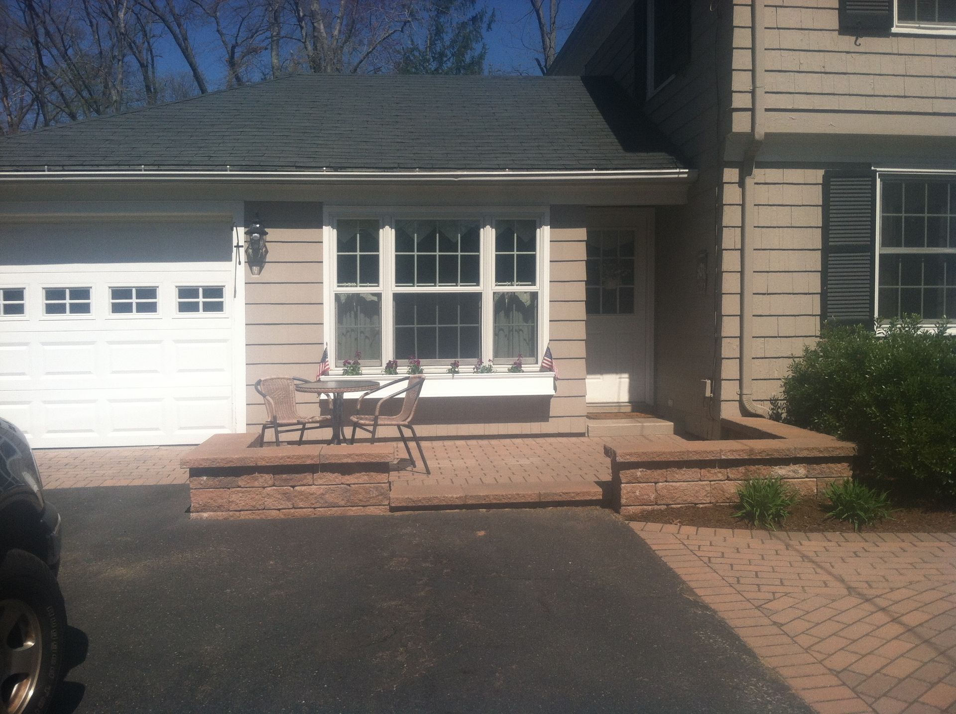 House exterior with brick porch, small table and chairs in front of a window, and a garage door.