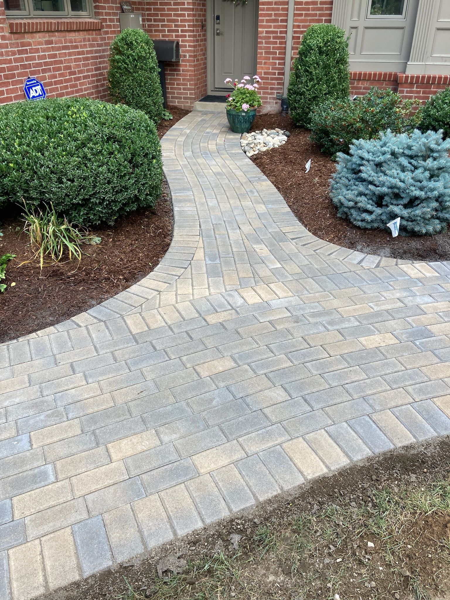 Brick pathway leading to a front door, lined with shrubs and mulch.