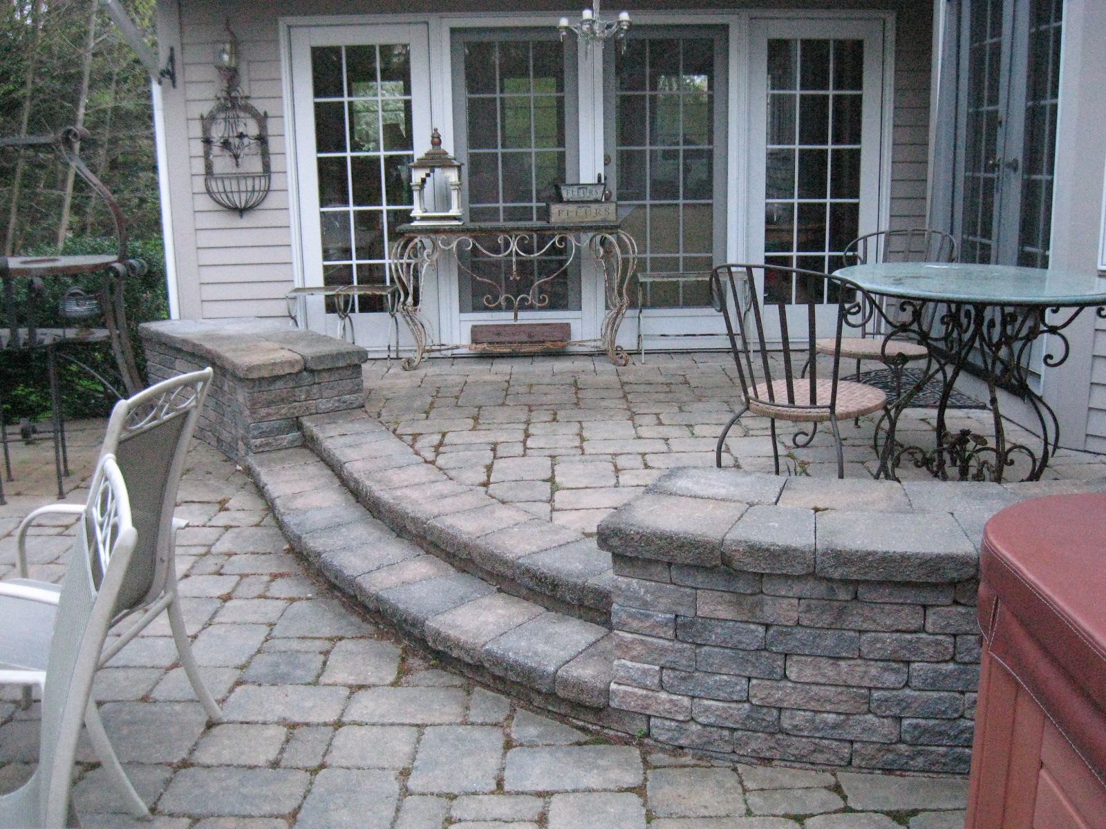Stone patio with steps leading to French doors, wrought iron furniture, and a hot tub.