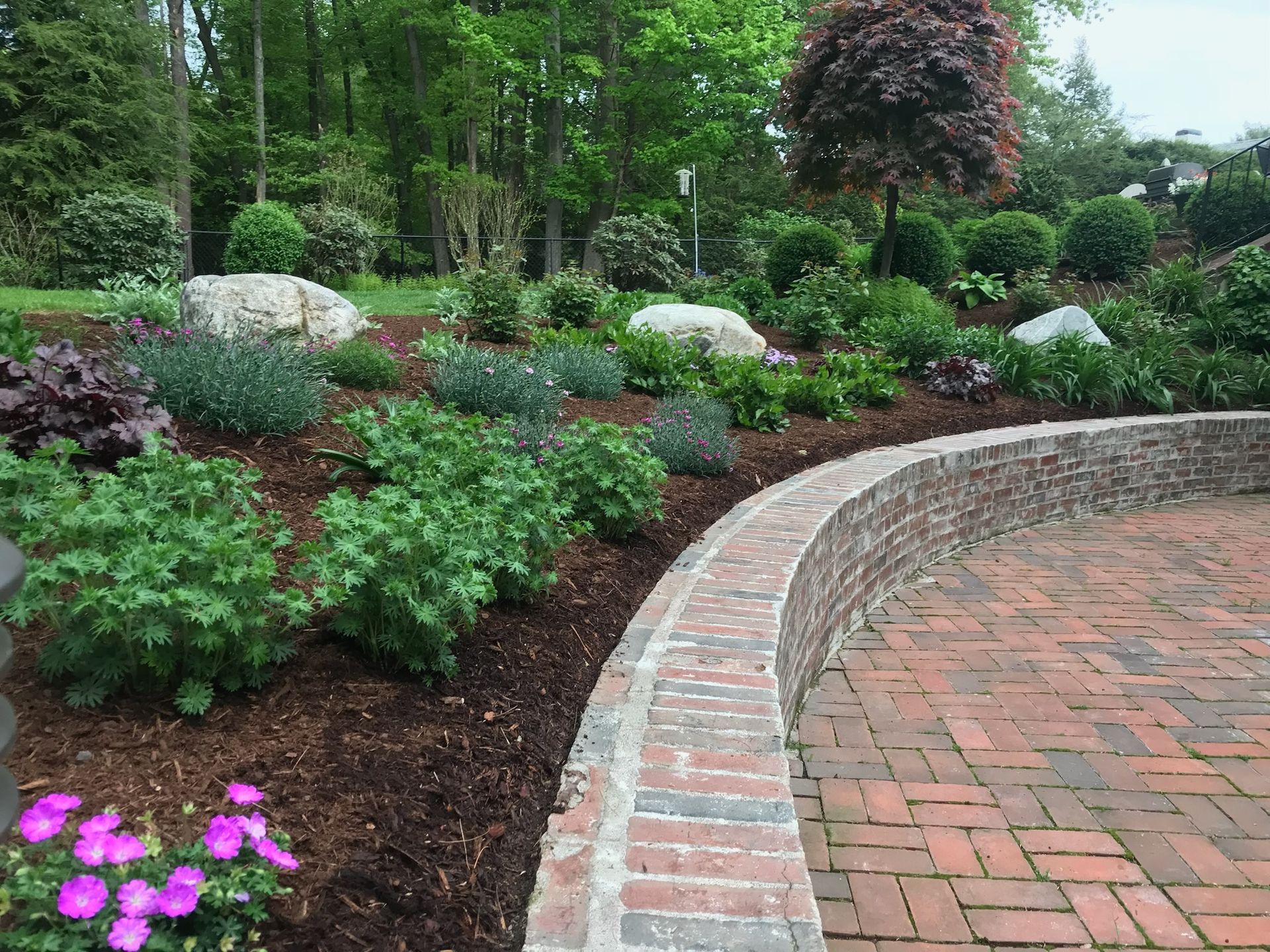 Finished landscape design project with brick patio, curved retaining wall, and tiered garden bed in Western MA