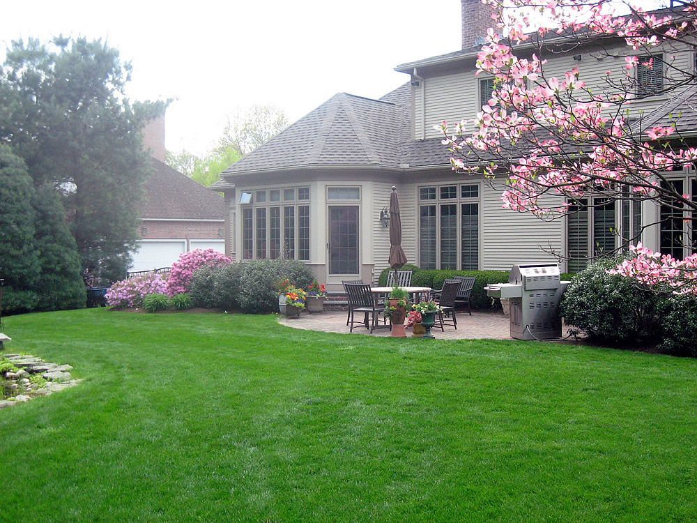 Lush green backyard with house, patio, and blooming pink tree.
