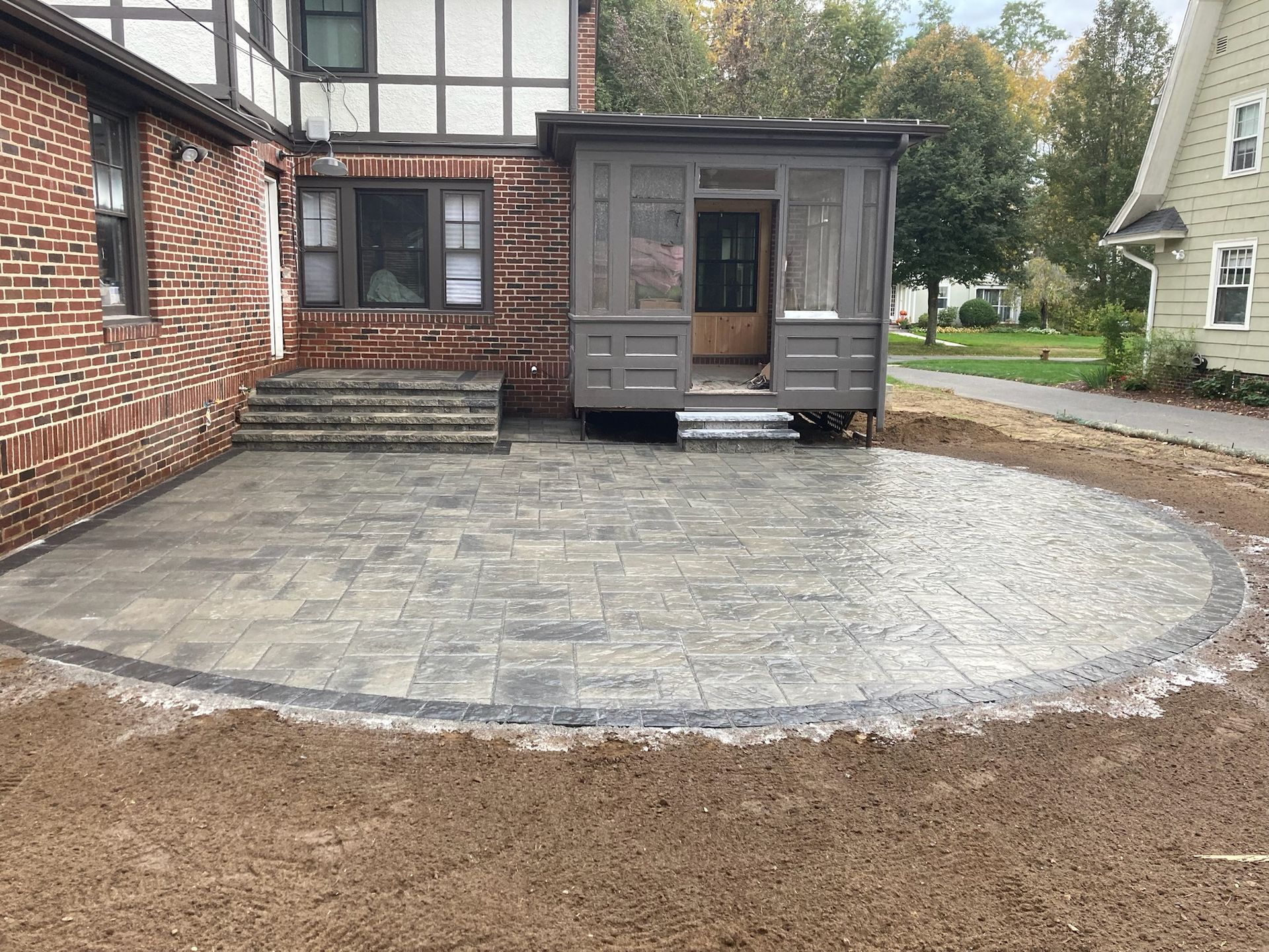 A newly constructed stone patio adjacent to a brick house, next to a screened porch.