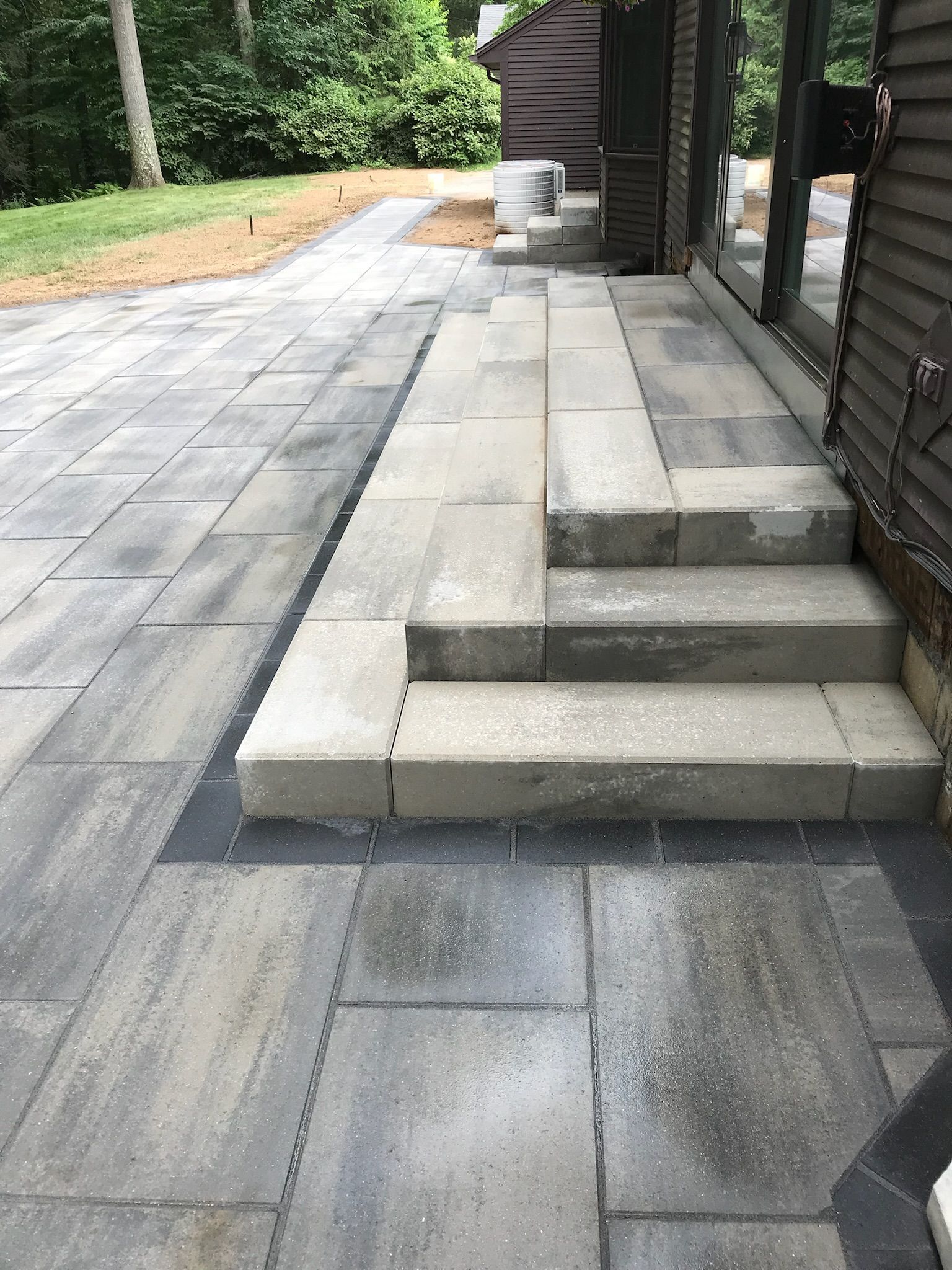 Paver patio and steps leading to a building with dark siding.