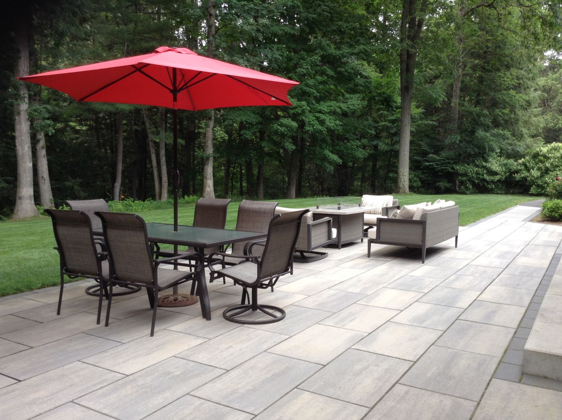 Patio with outdoor furniture, including a red umbrella and dining set, surrounded by trees.