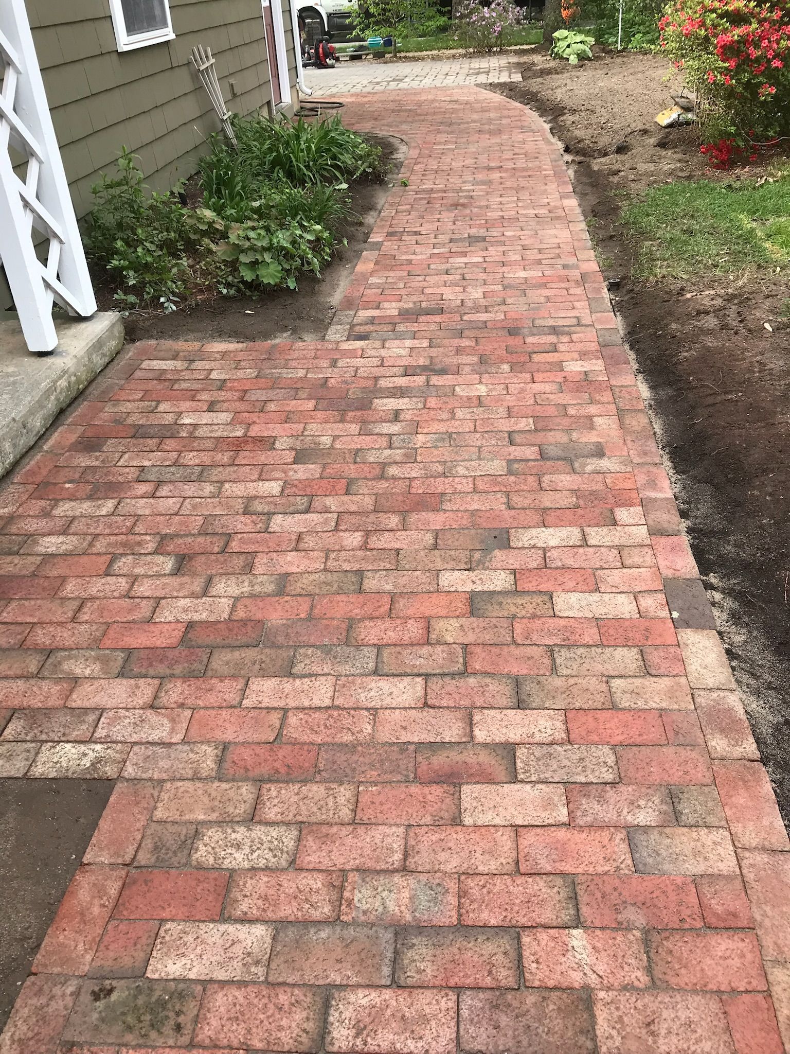 Brick pathway leading to a building, bordered by greenery, red and brown bricks.