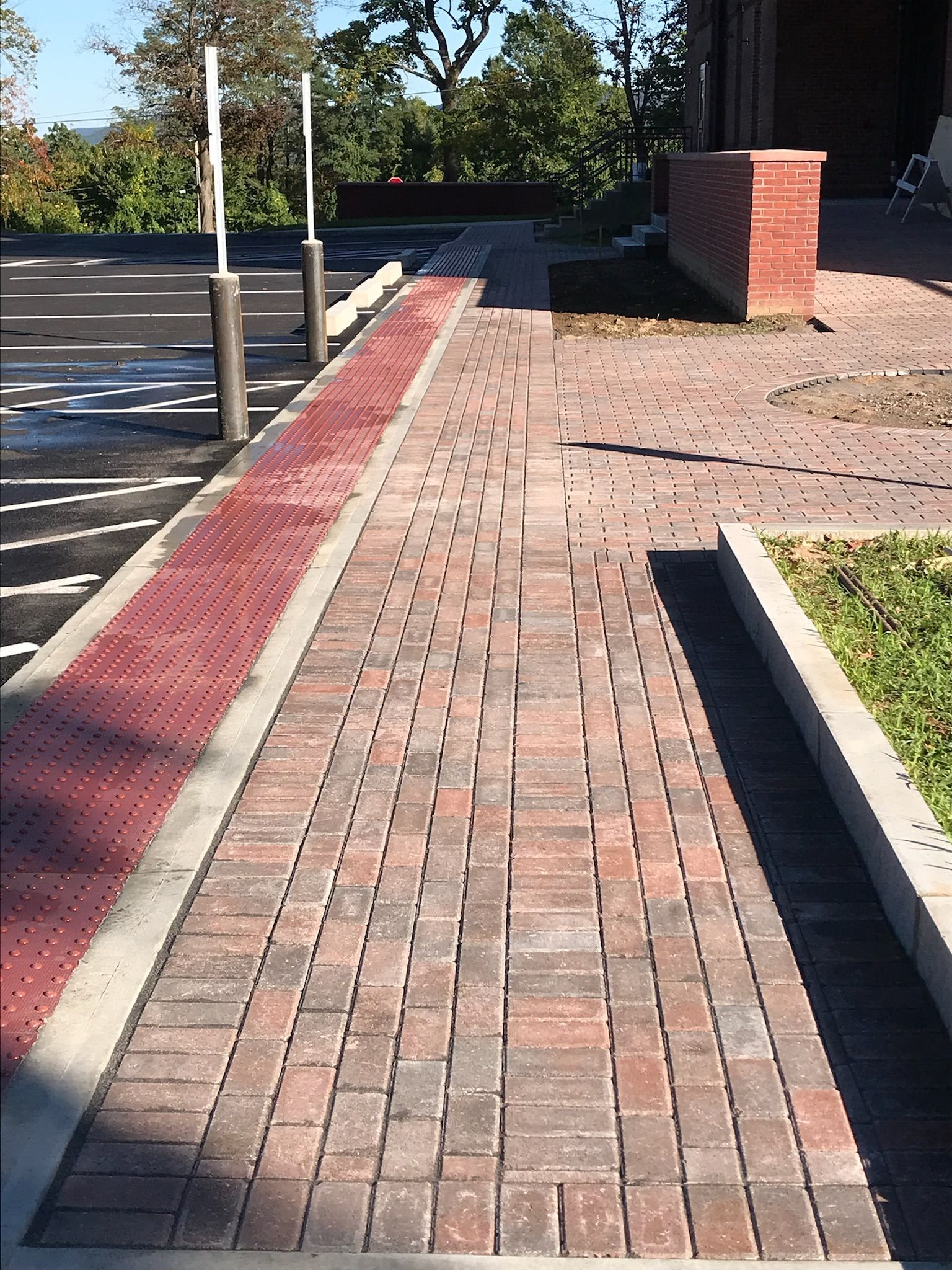 Brick walkway with red tactile paving, leading to a building, and parking lot.
