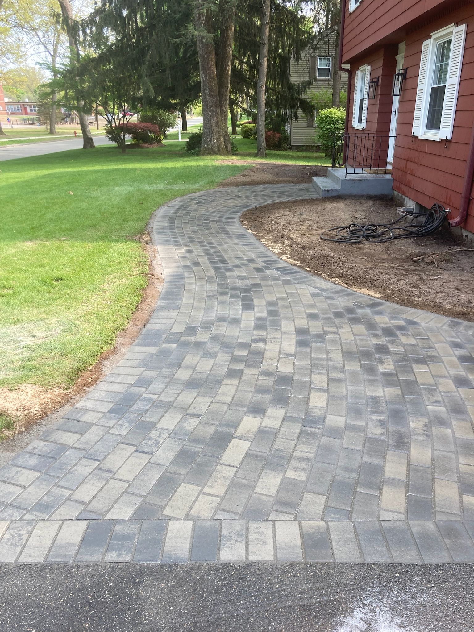 Brick pathway curving from a road to a red house, alongside grass.