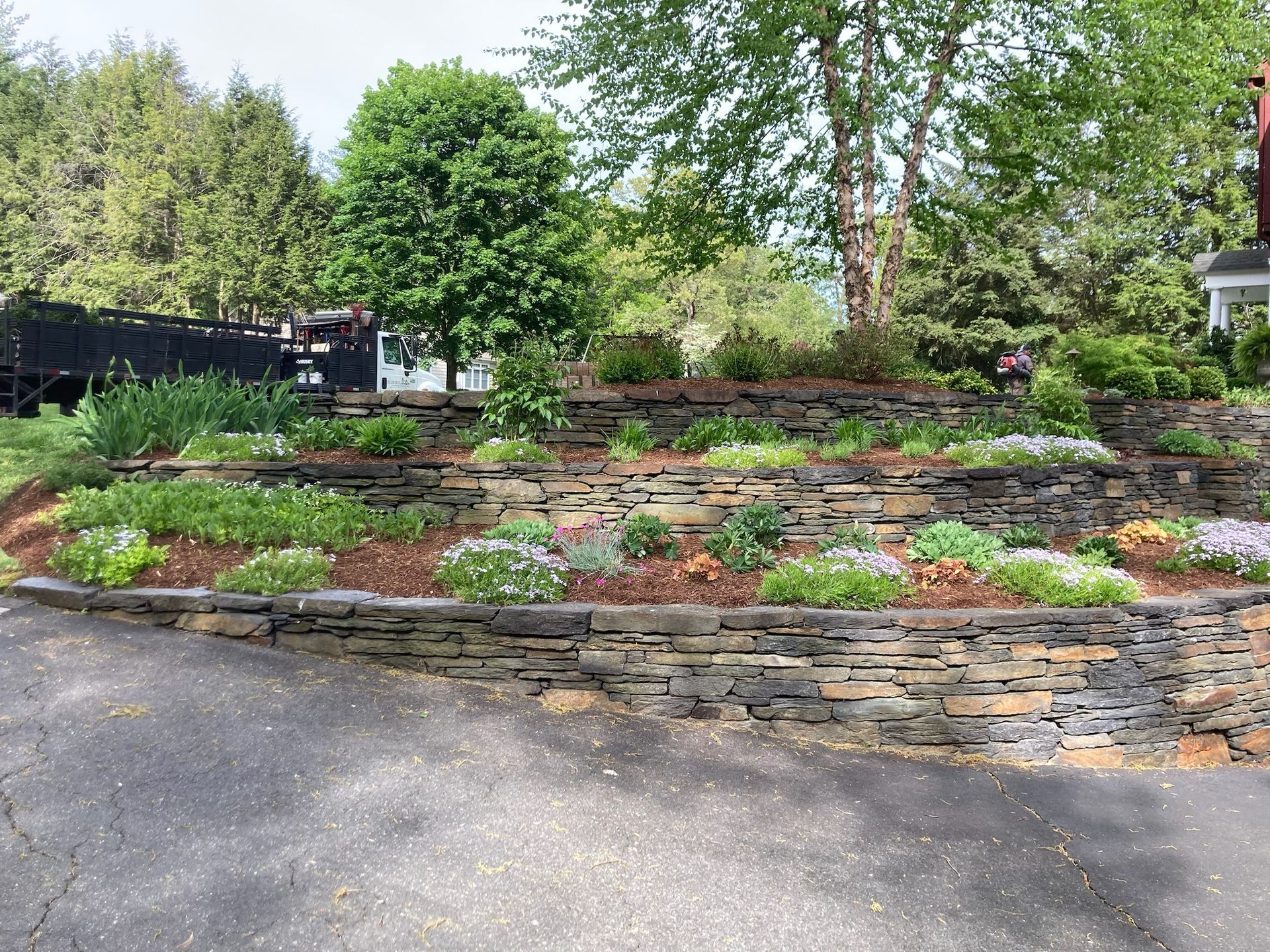 Stone retaining walls with tiered landscaping and flowers along a driveway.