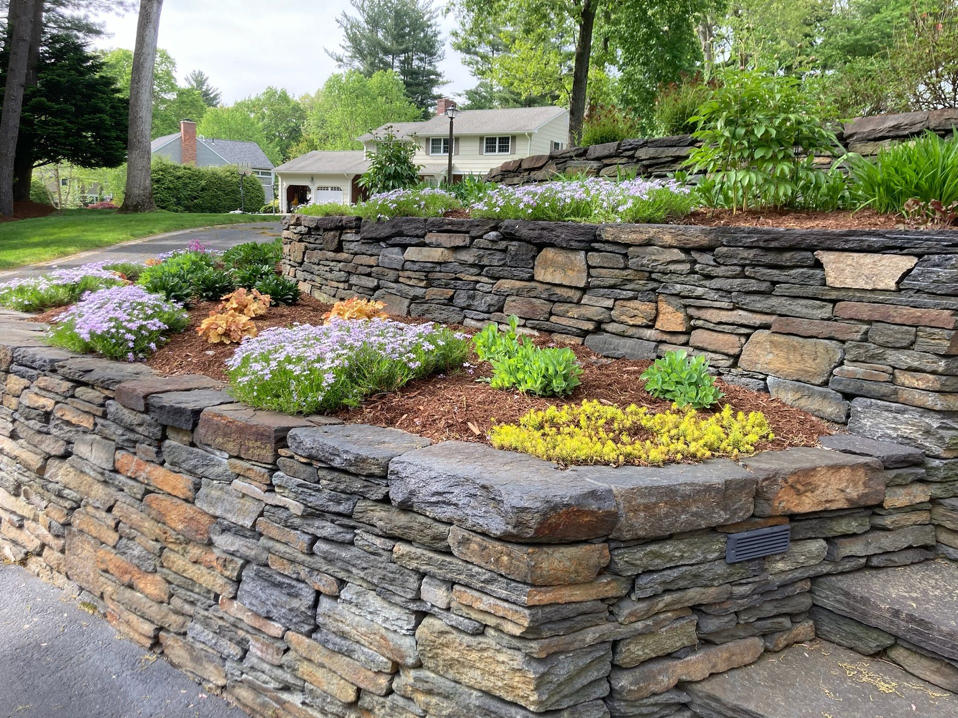 Stone retaining walls with colorful flowers and mulch in a residential garden.