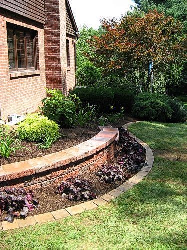 Brick retaining wall with flower bed bordering a lawn and house.