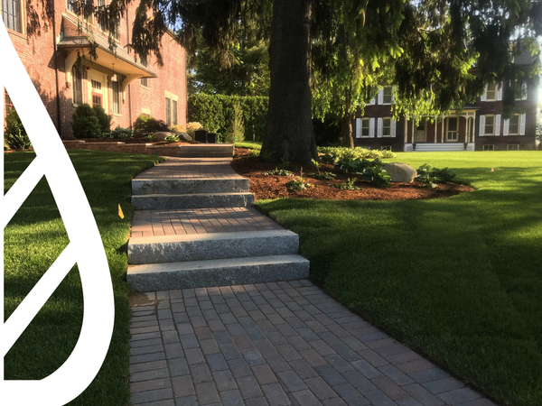 Stone steps and brick pathway leading up to a large house with a lush green lawn.