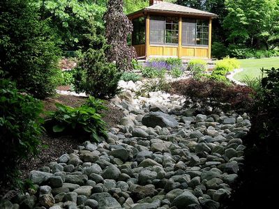 Dry creek bed leading to a gazebo in a lush garden.