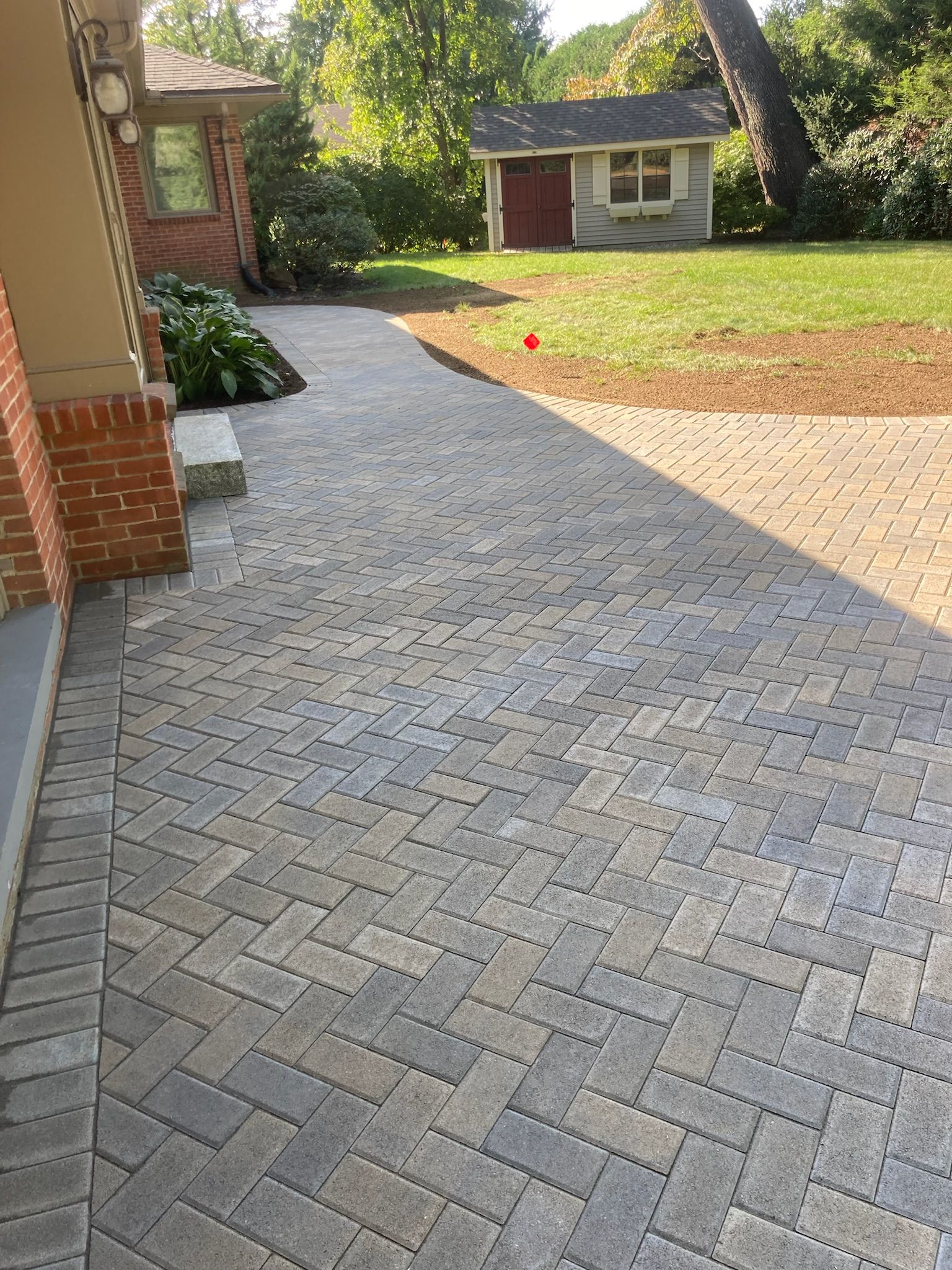 Brick walkway leading to a small shed, lawn on the right, brick and stone exterior on the left.