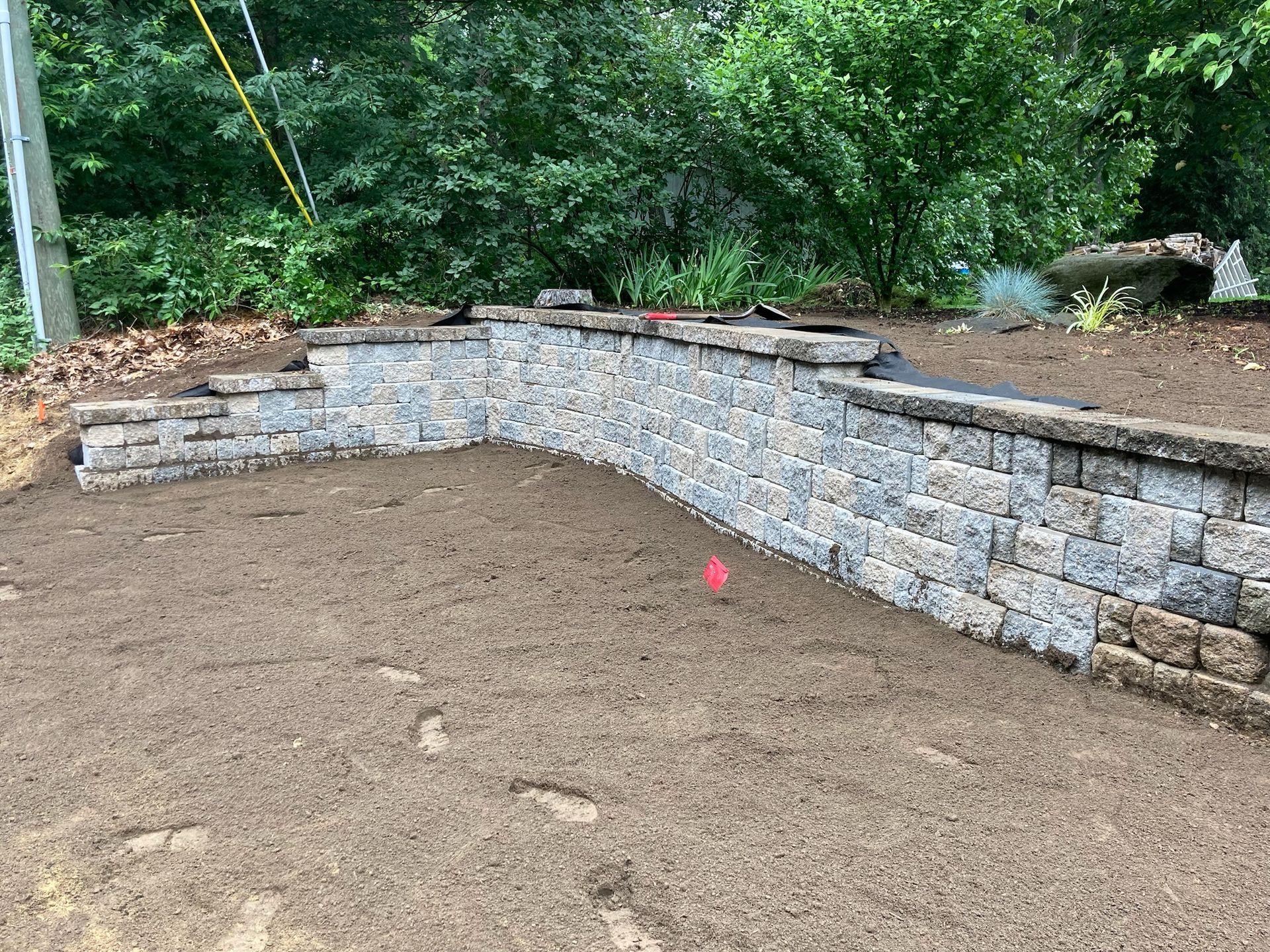 Stone retaining wall with steps and freshly tilled dirt in a yard setting.