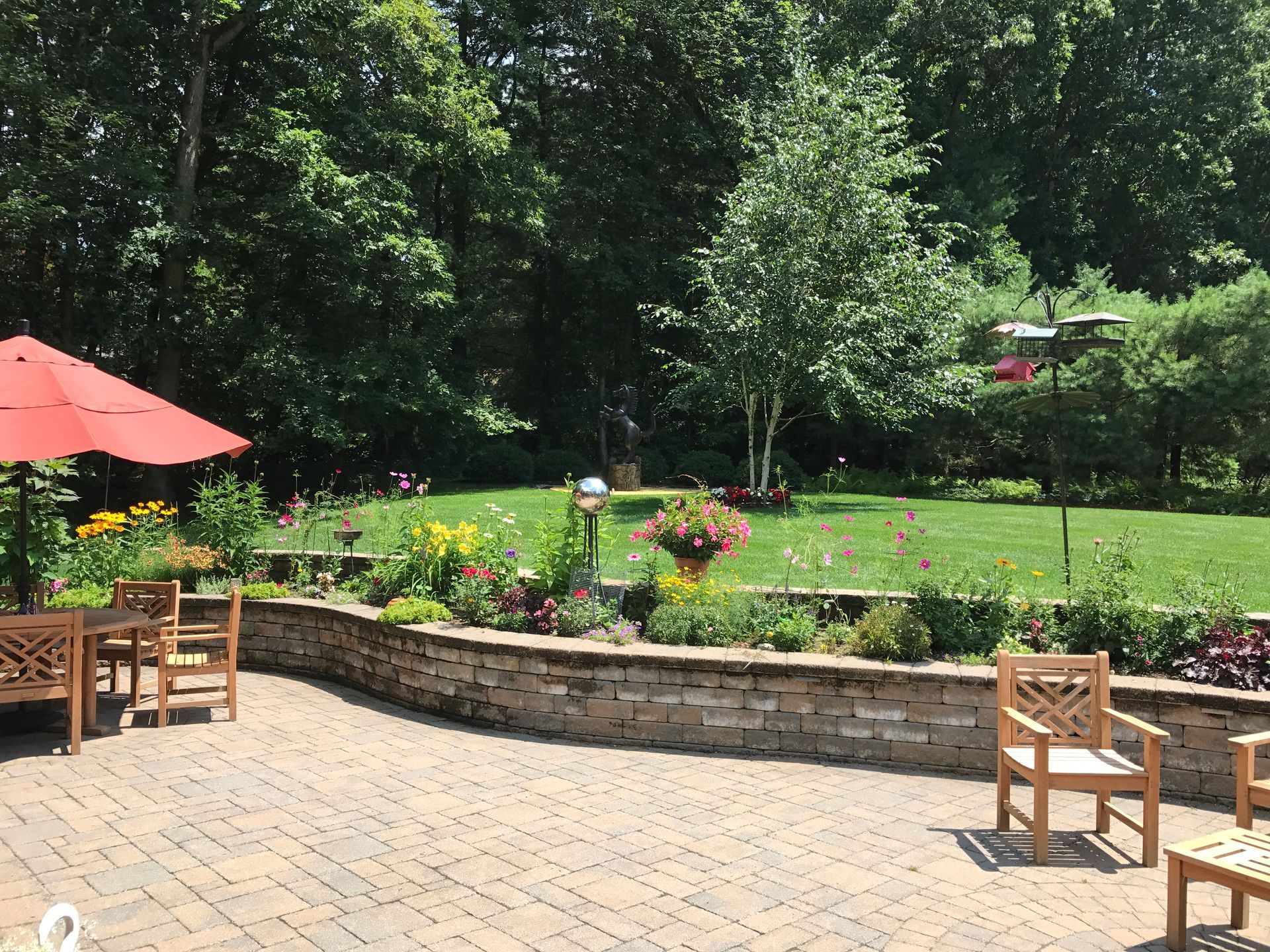 Patio with wood furniture, red umbrella, and flower beds overlooking a grassy yard with trees.
