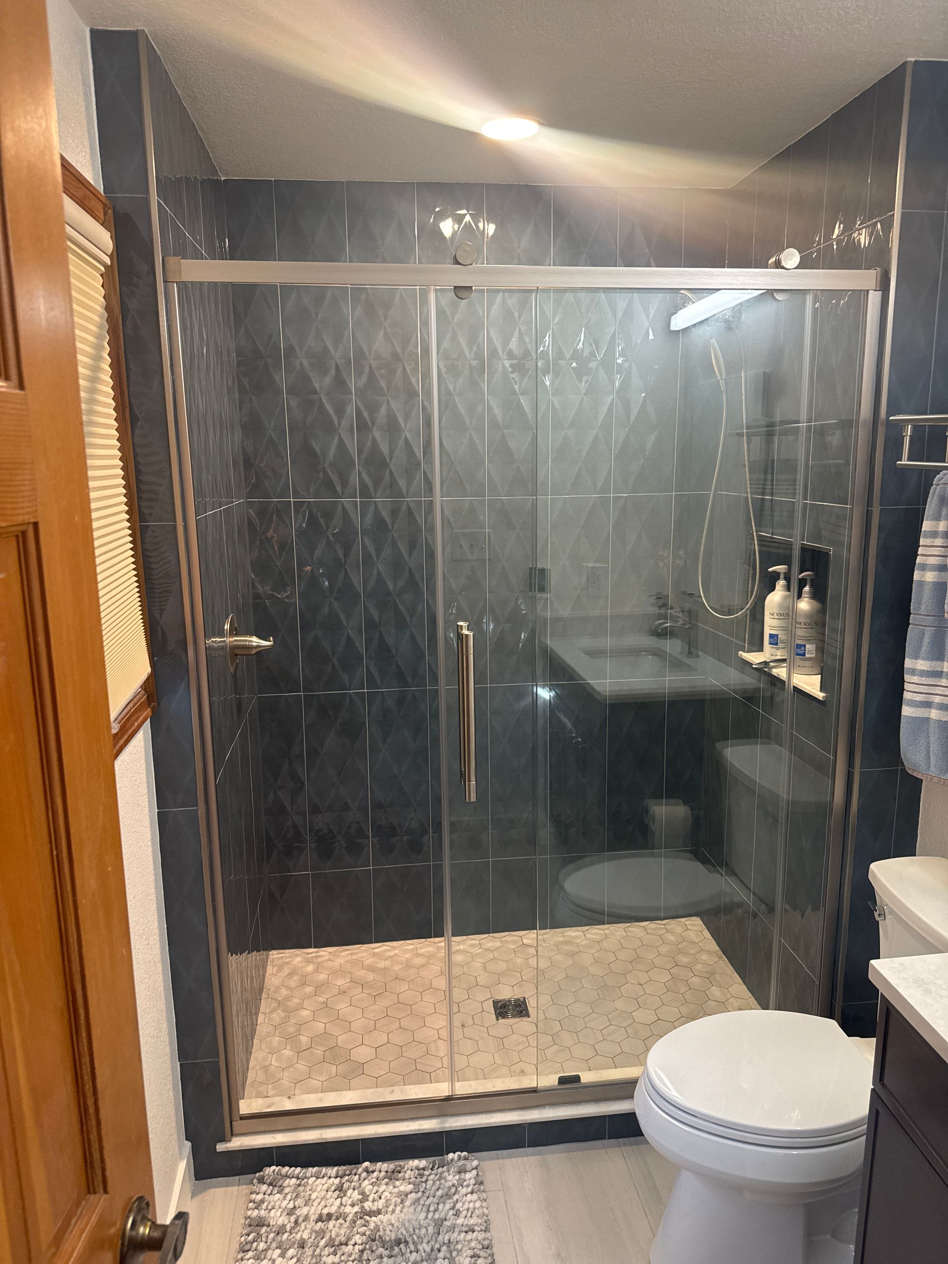 Bathroom with a glass-enclosed shower, dark tile walls, beige floor, and a toilet in the foreground.