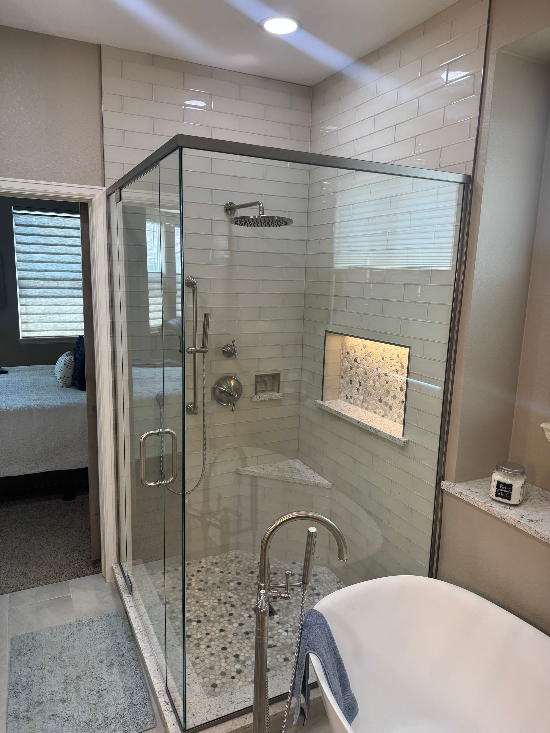 Bathroom with glass shower enclosure, beige tiled walls, and white vanity beside a bed.