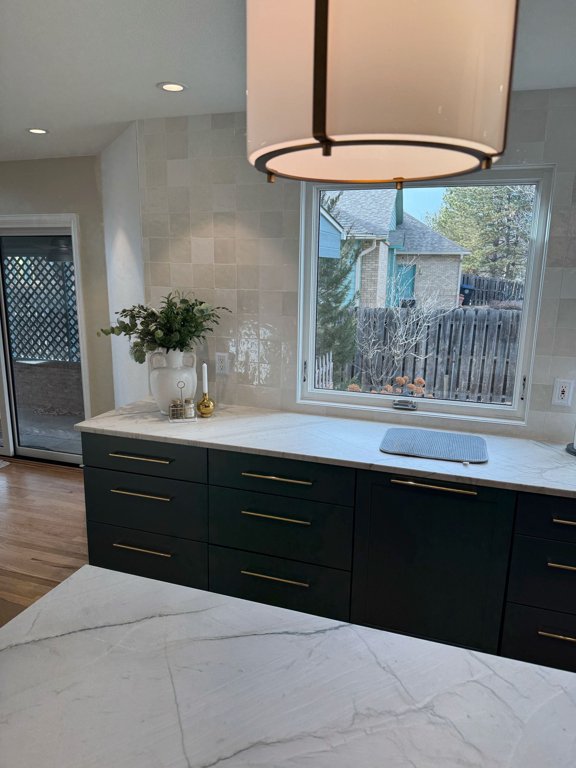Modern kitchen with dark cabinets, marble island, pendant light, and a window over the sink