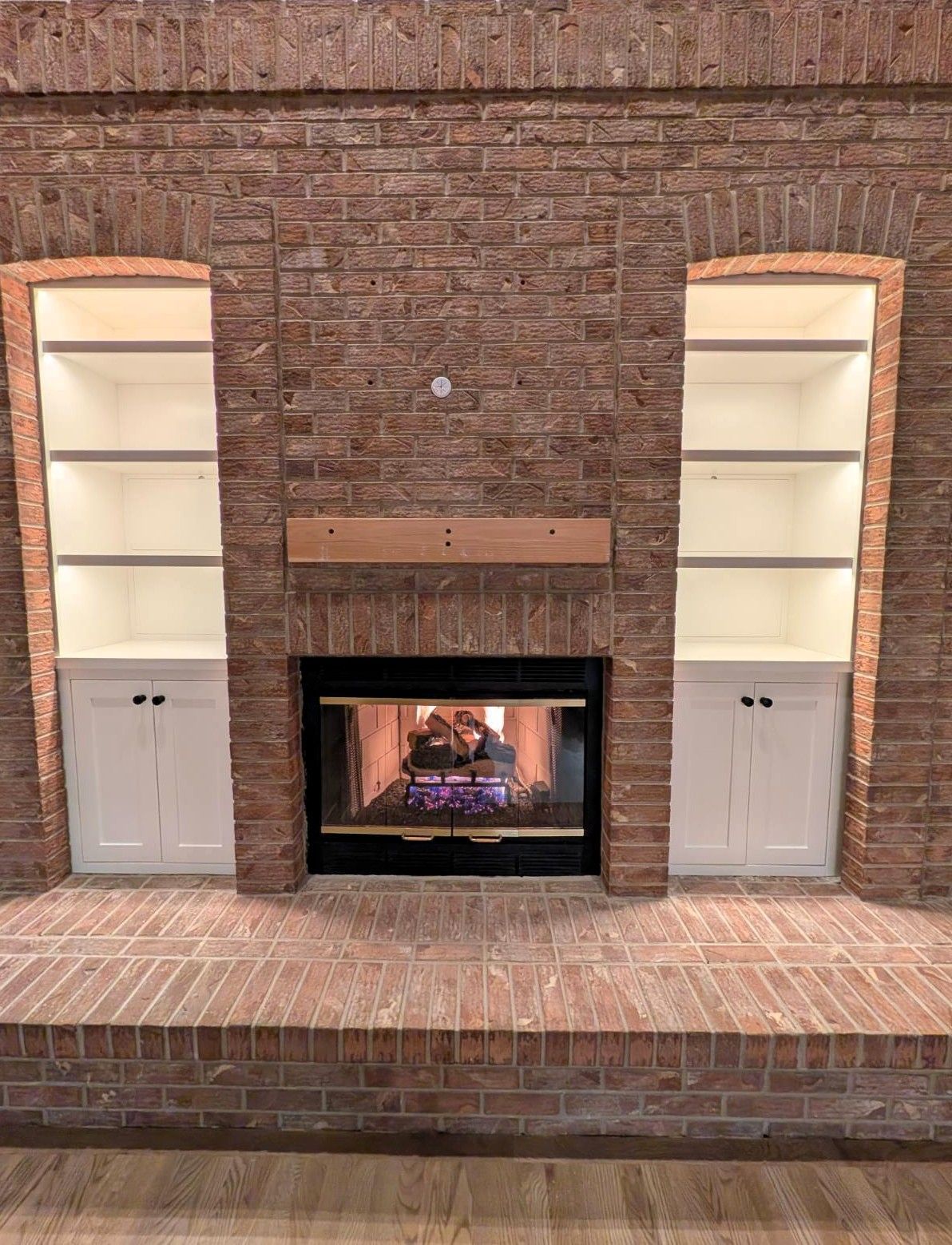 Built-in brick fireplace with TV niche, white cabinets, and shelves on either side