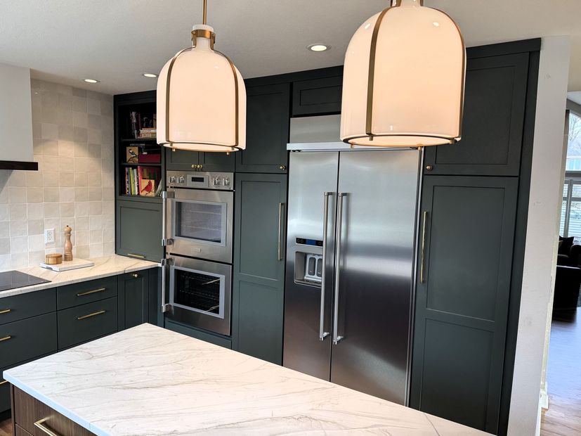 Modern kitchen with white island, dark cabinets, stainless steel fridge, and two pendant lights