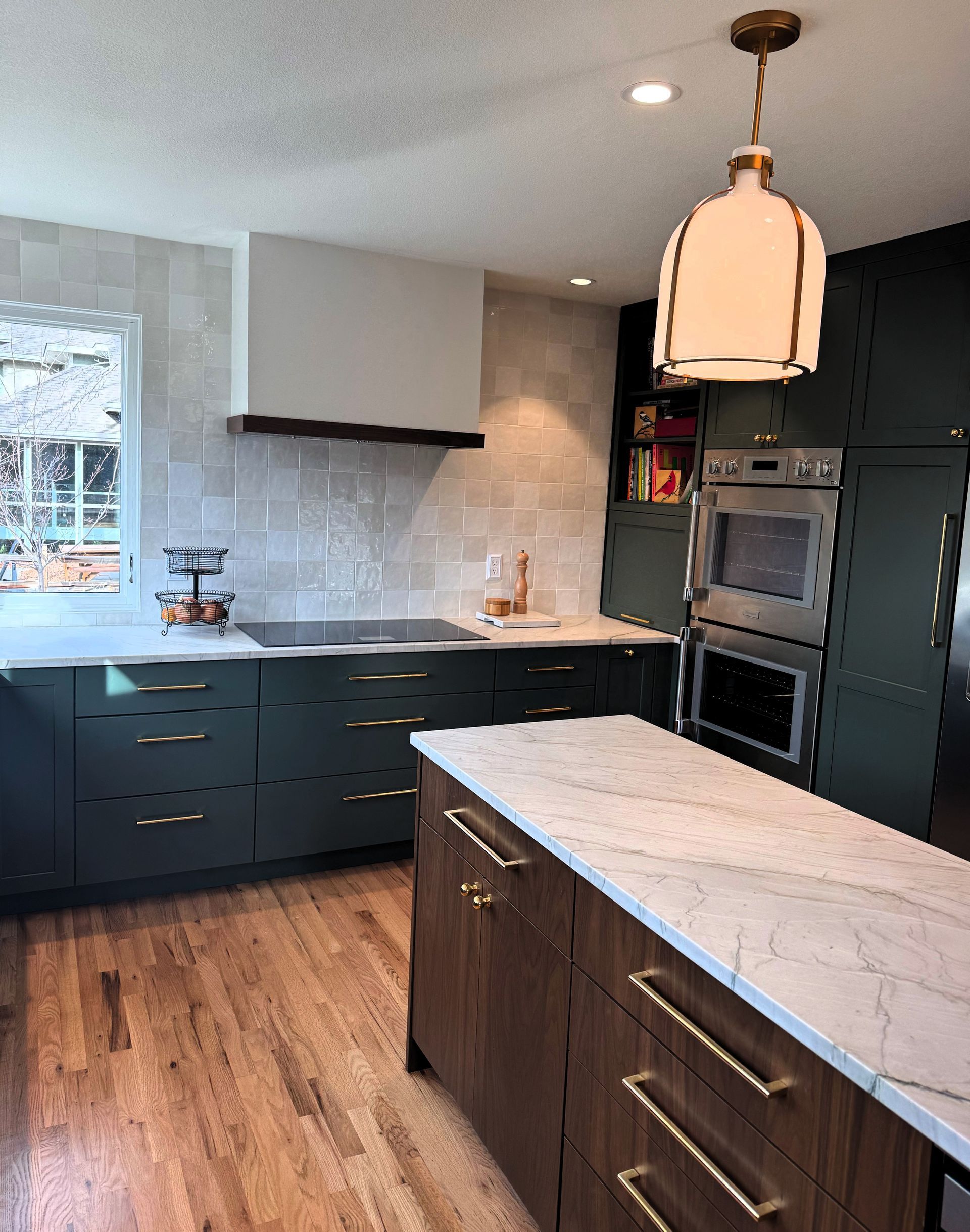 Modern kitchen with dark cabinets, white countertops, wood floor, and a central island under pendant lights