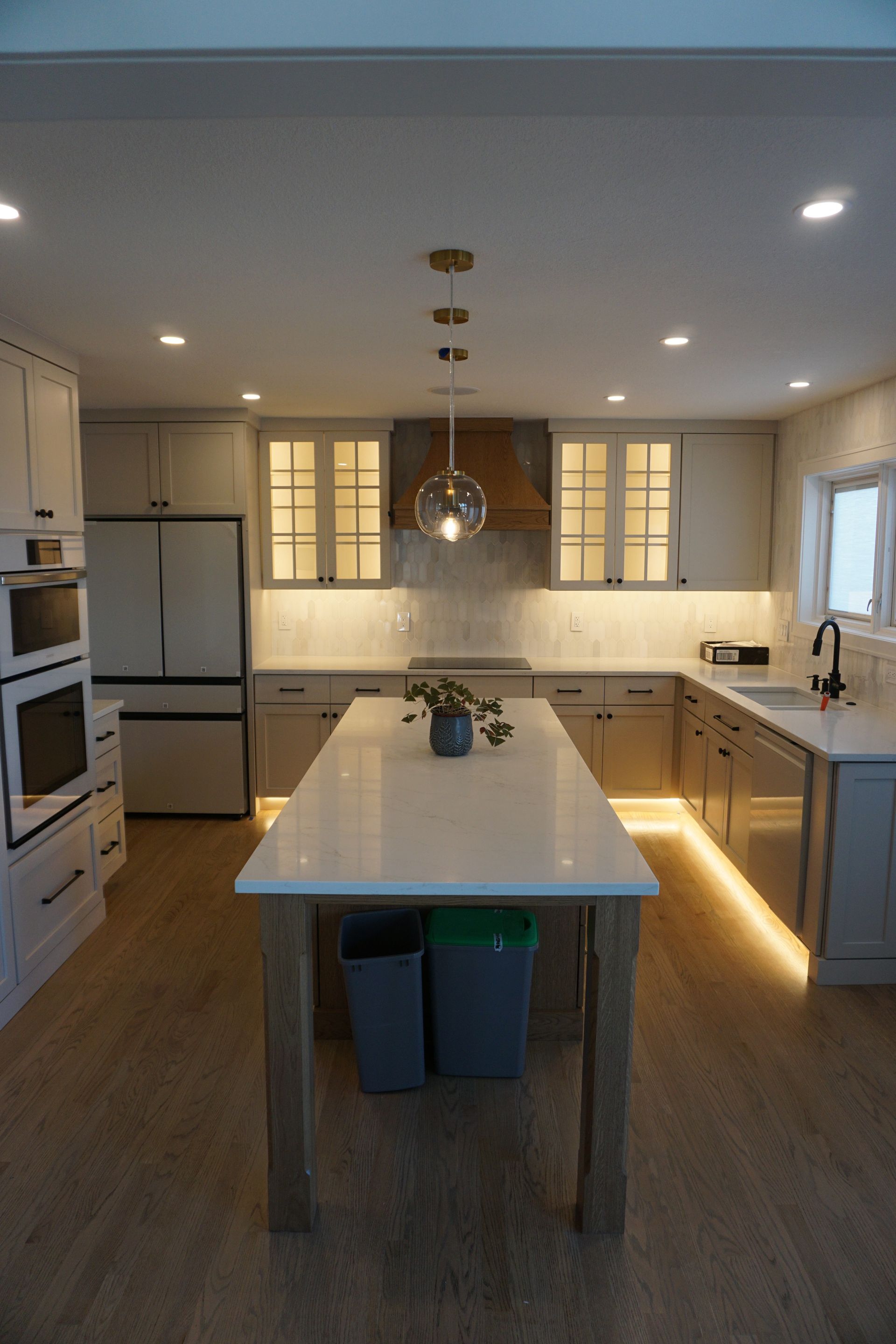 Modern white kitchen with island, pendant light, stainless appliances, and warm under-cabinet lighting