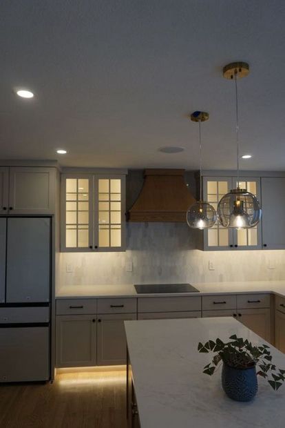 Modern kitchen with gray cabinets, wood range hood, pendant lights, and a white island with a plant.