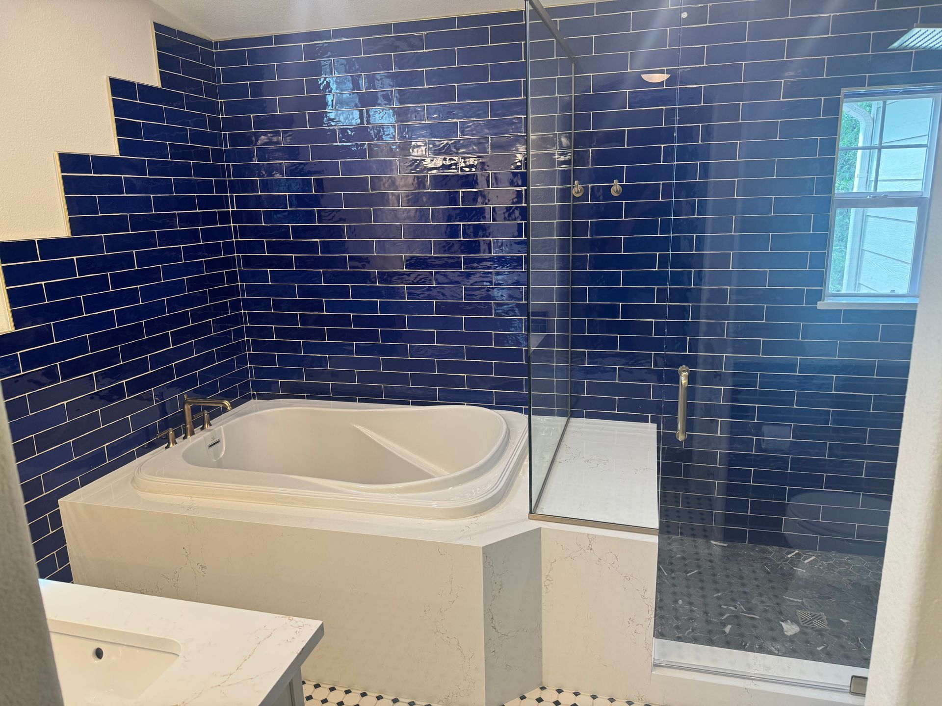 Blue-tiled bathroom with a white corner soaking tub and glass shower enclosure