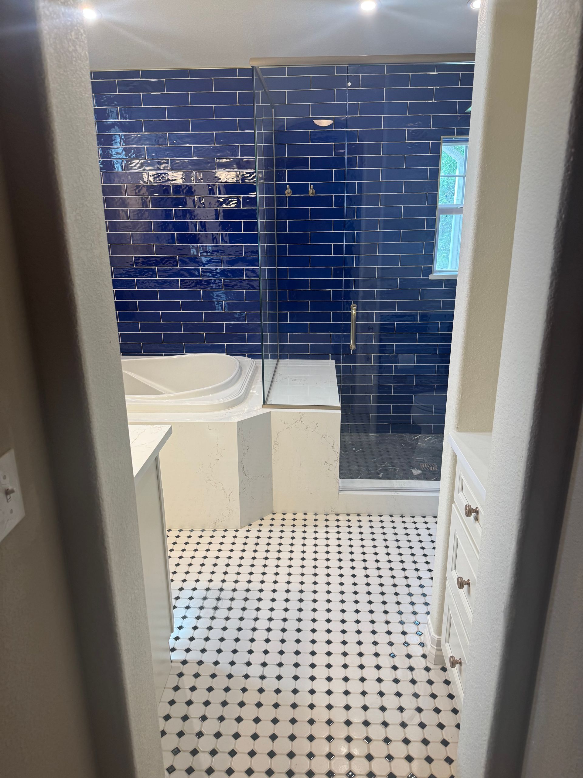 Bathroom with white tiled floor, blue tiled shower wall, and a white bathtub sink area.