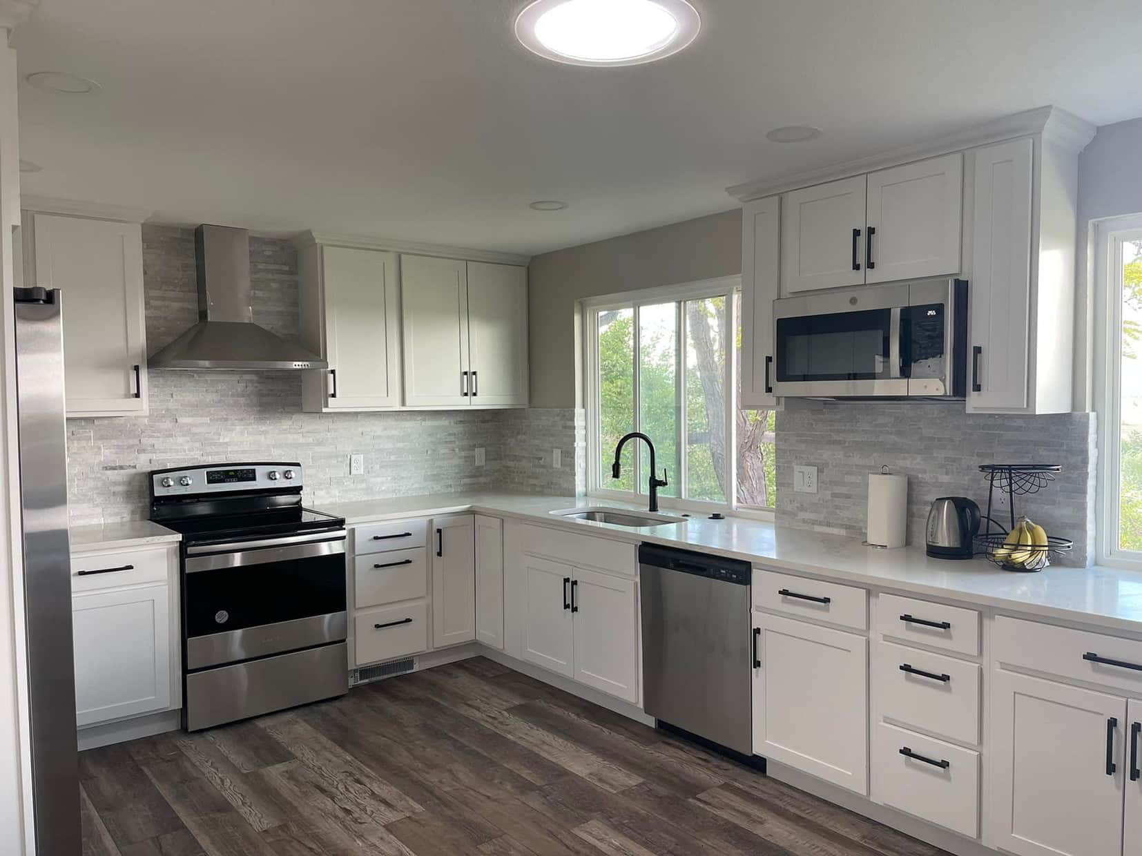 Bright modern kitchen with white cabinets, stainless steel appliances, and wood flooring