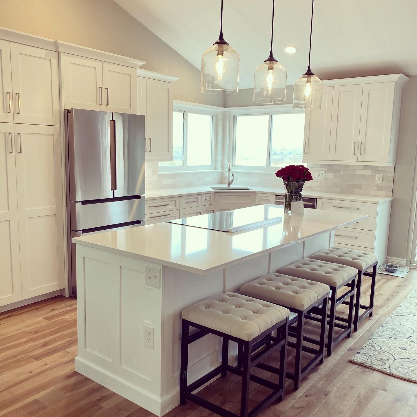Bright white modern kitchen with island, stools, stainless fridge, and pendant lights