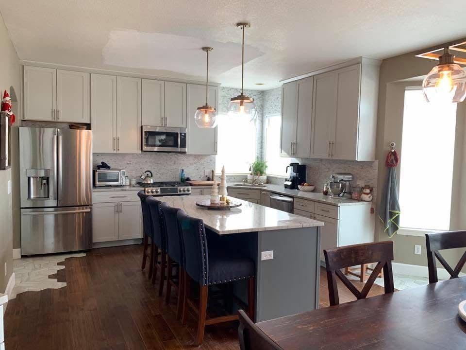 Bright modern kitchen with stainless steel appliances, gray cabinets, island seating, and pendant lights