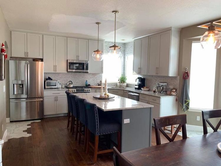 Bright modern kitchen with gray cabinets, stainless appliances, island seating, and dark wood floors