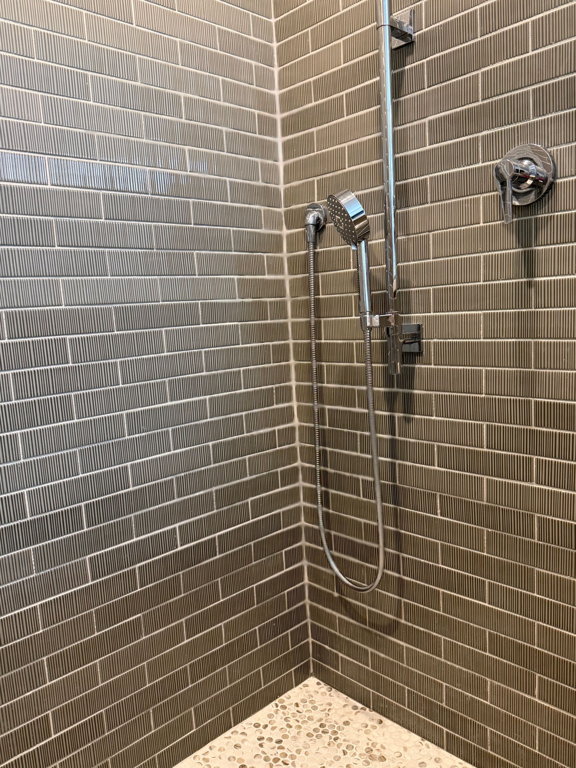 Tiled shower corner with chrome showerhead and controls, beige and brown mosaic walls and floor.