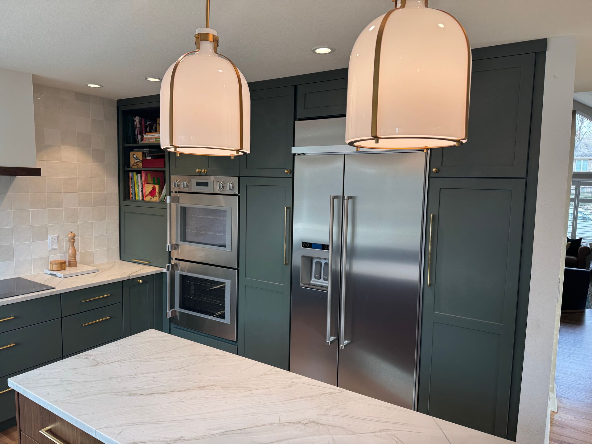 Modern kitchen with stainless steel refrigerator, built-in ovens, dark cabinets, and two pendant lights