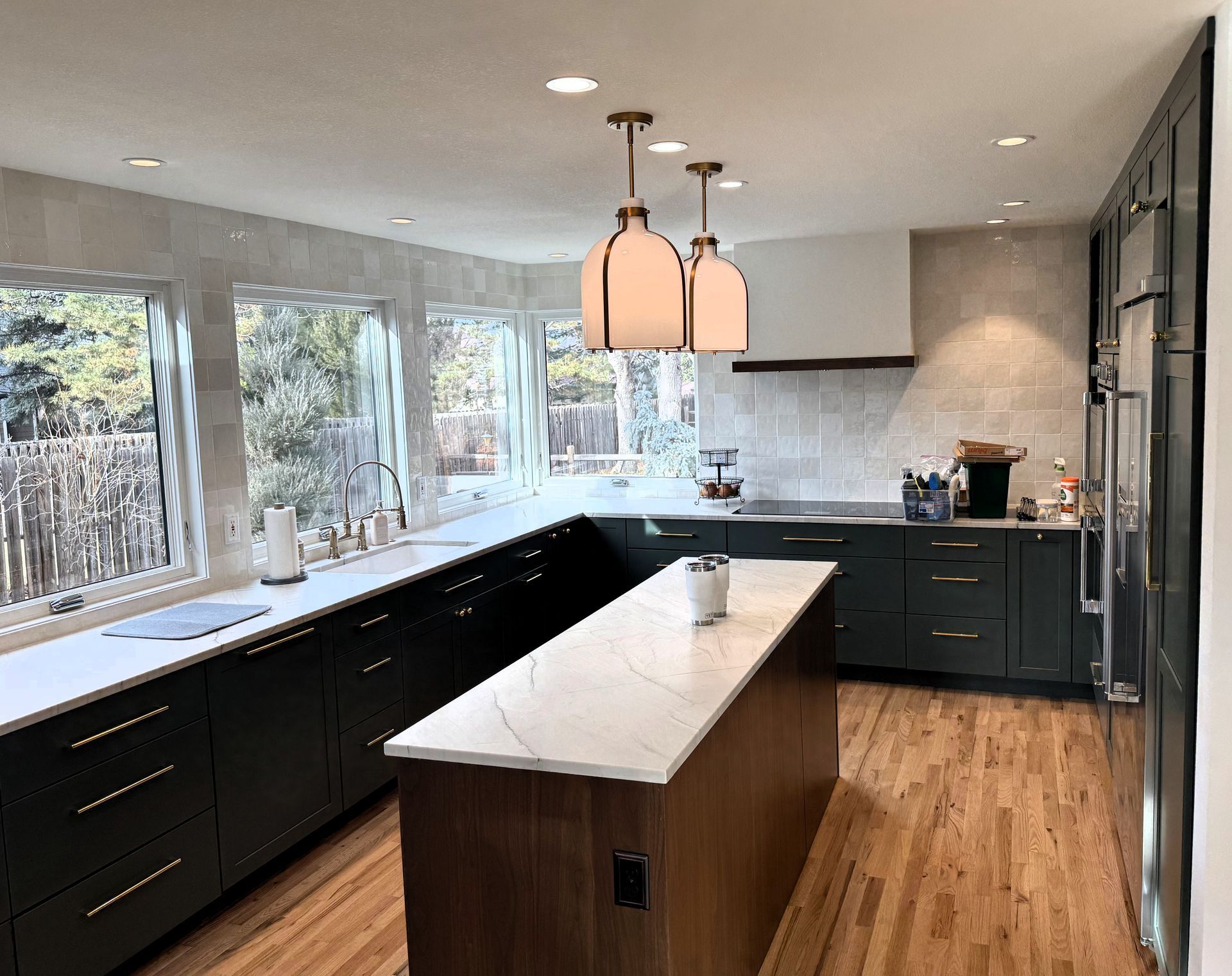 Modern kitchen with dark cabinets, white island, pendant lights, and large windows overlooking trees