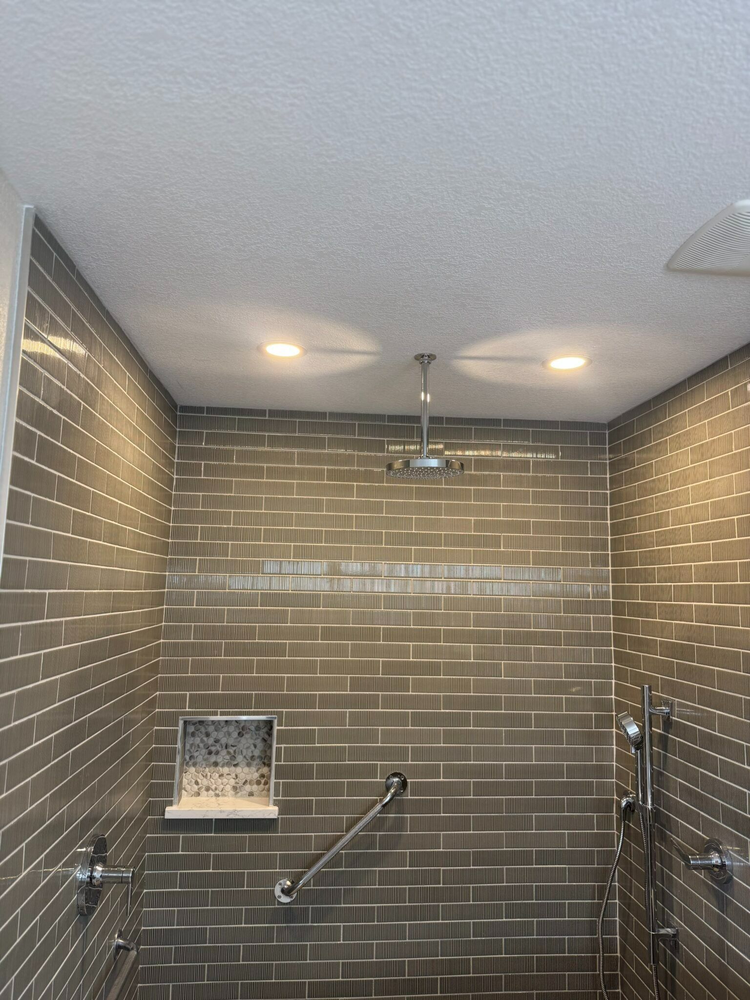 Modern tiled shower with rainfall showerhead, niche shelf, and glass divider in a bathroom