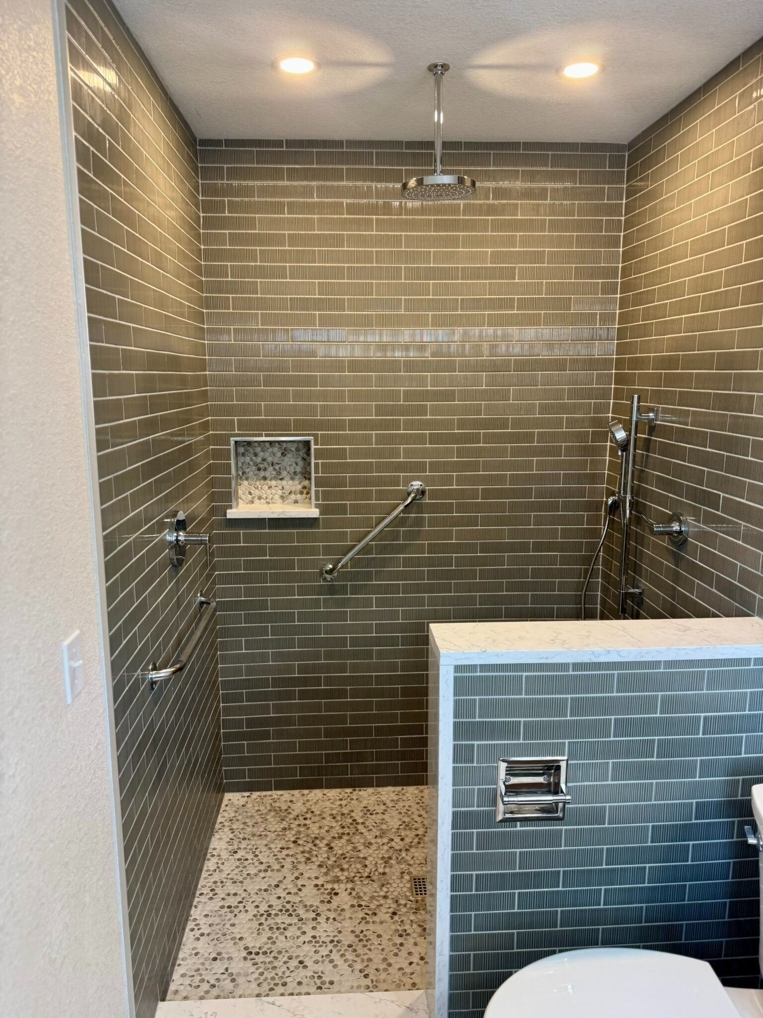 Small modern shower with gray tile walls, multiple grab bars, and a white-tiled bench.