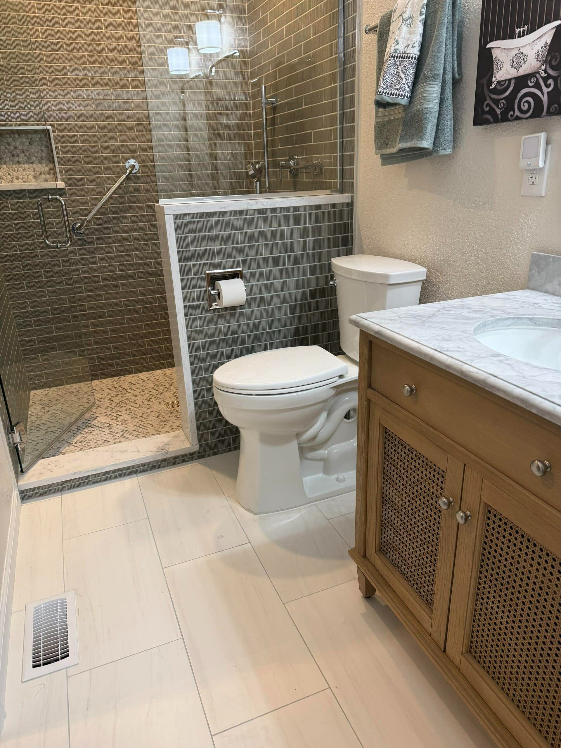 Bathroom with glass shower, toilet, vanity, and tiled floor in beige and gray tones