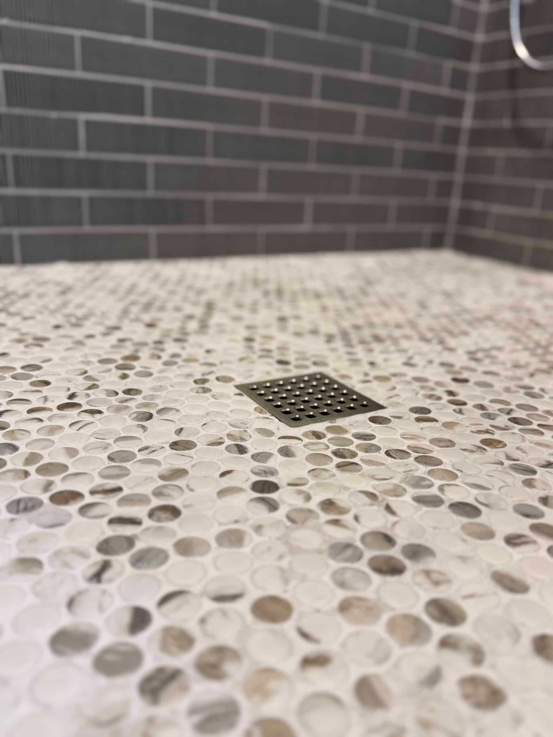 Pebble-patterned shower floor with a small square drain against a gray brick wall