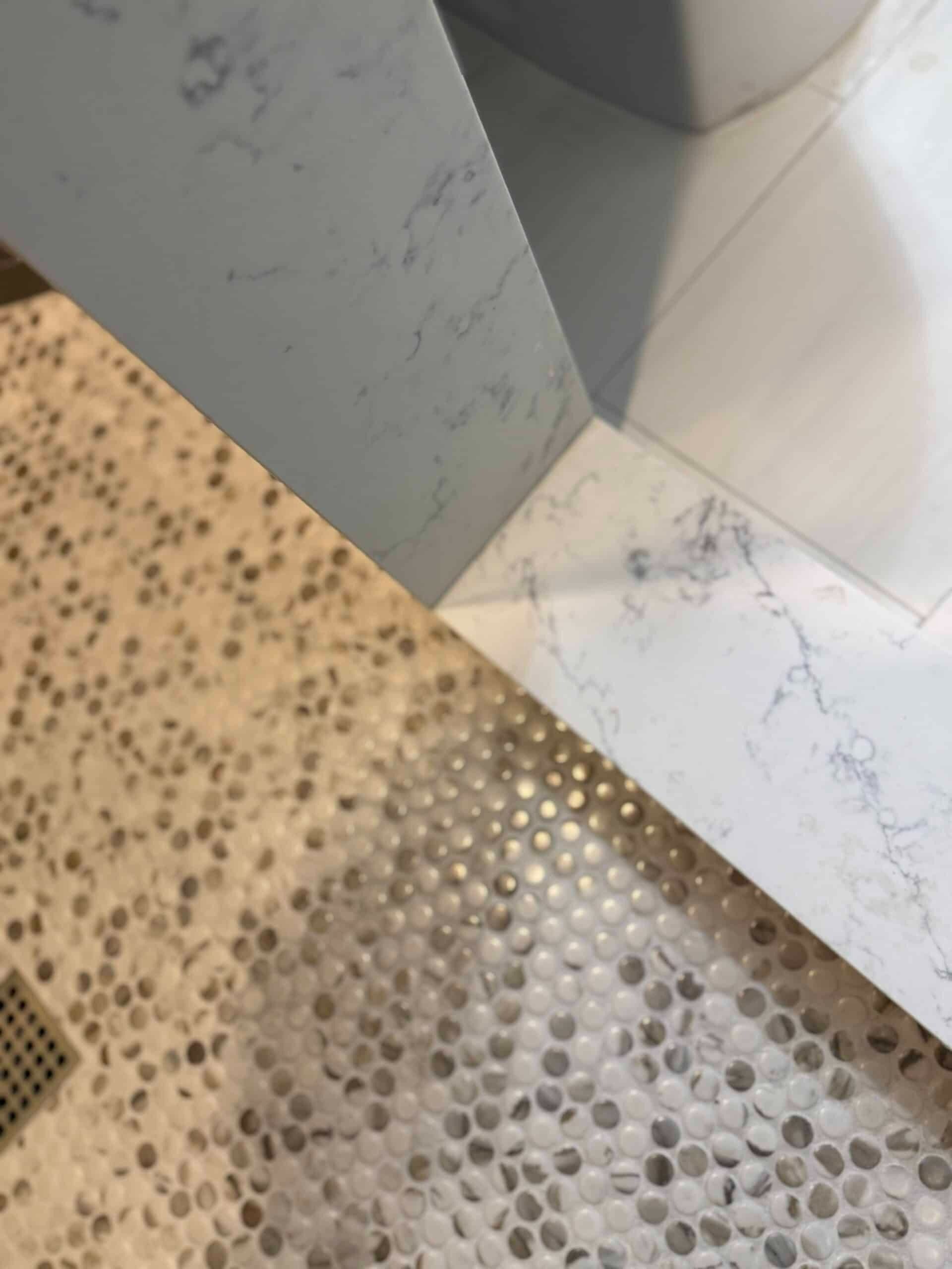 Mosaic bathroom floor with tan and gray pebble tiles beside a white marble threshold and wall corner