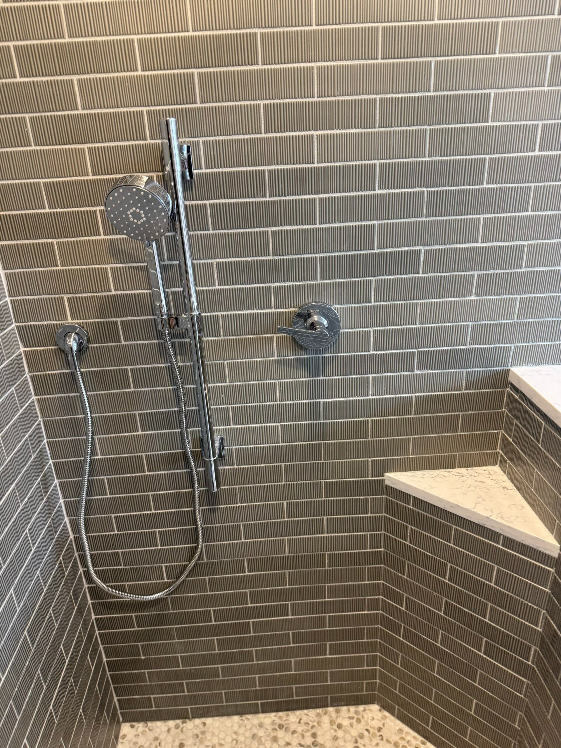 Accessible shower with handheld showerhead, grab bars, and a built-in bench on textured tile walls