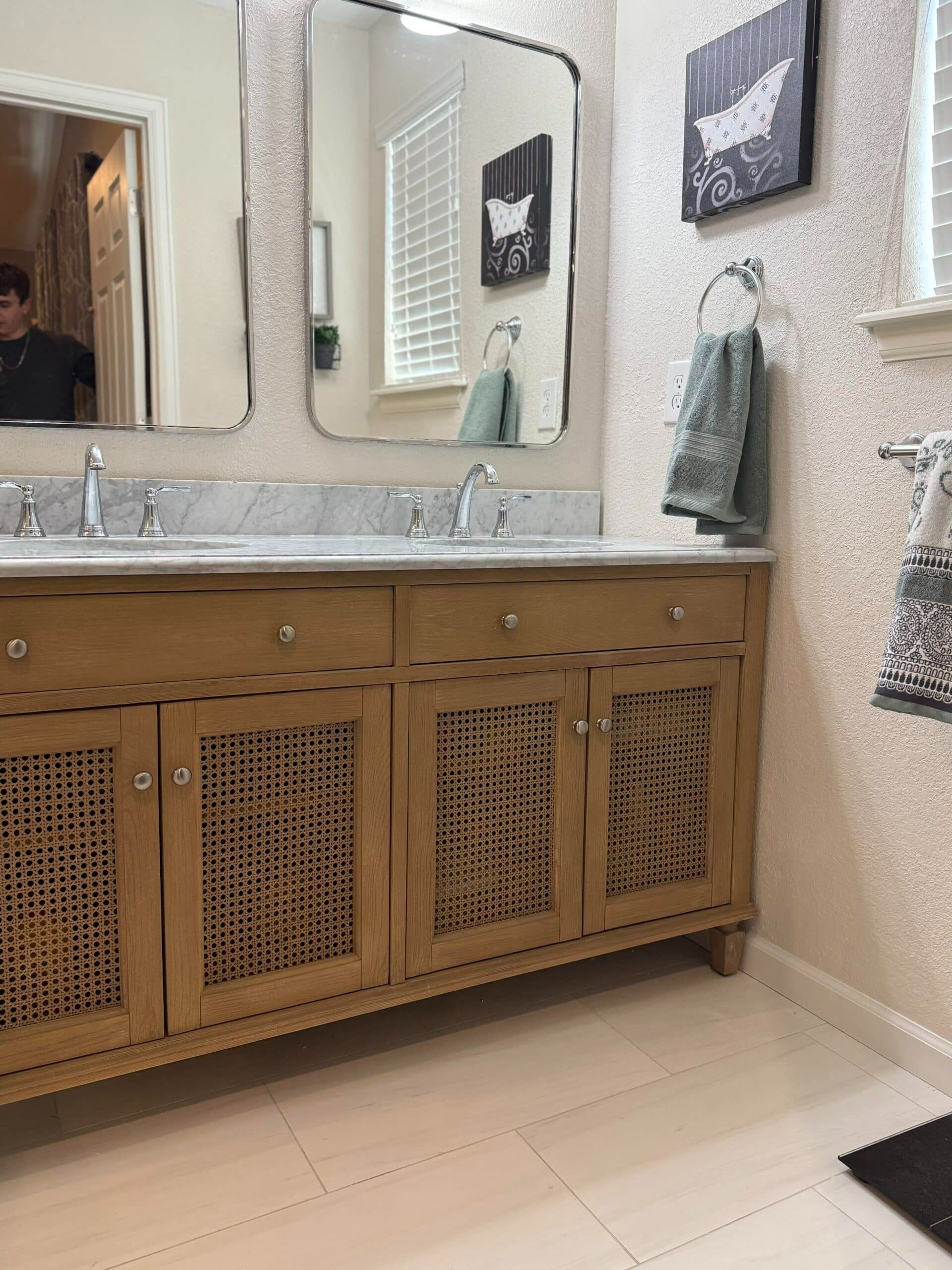 Bathroom vanity with double mirrors, wood cabinet, and towels on a beige wall.