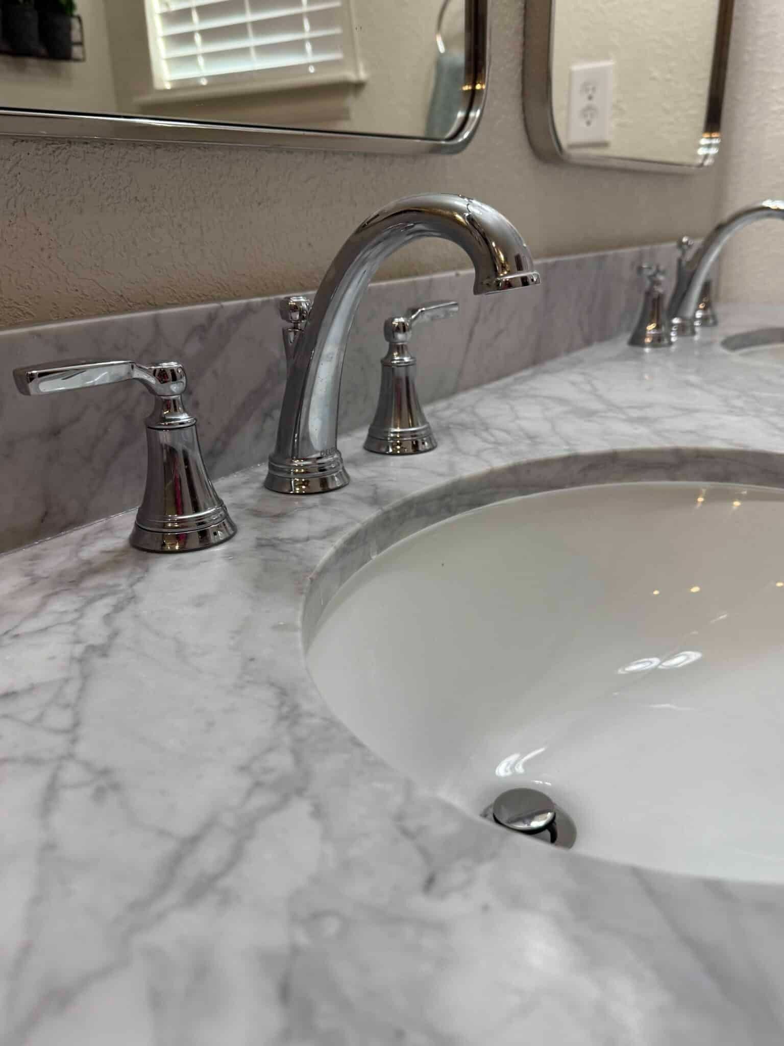 Marble bathroom vanity with chrome faucet and sink mirror in the background