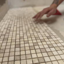 Hand placing white mosaic tiles on a tiled floor in a room under construction