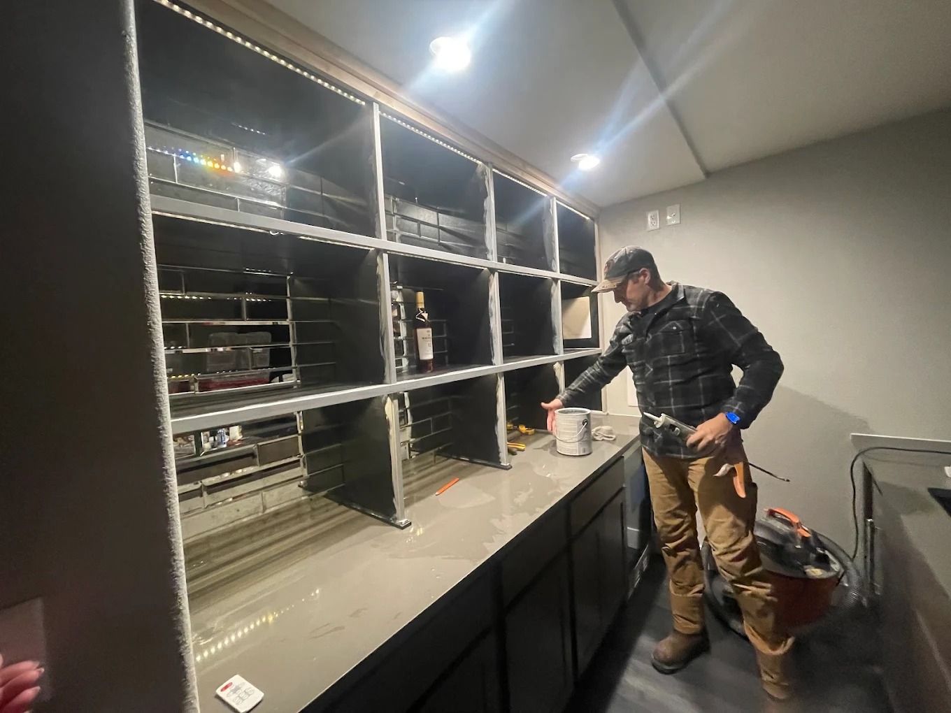 Worker inspecting a black cabinet in a garage with open shelving and a bright overhead light