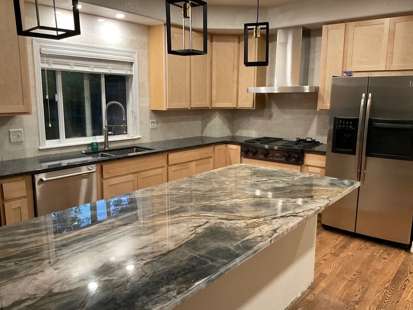 Modern kitchen with marble island, wood cabinets, stainless appliances, and window above the sink