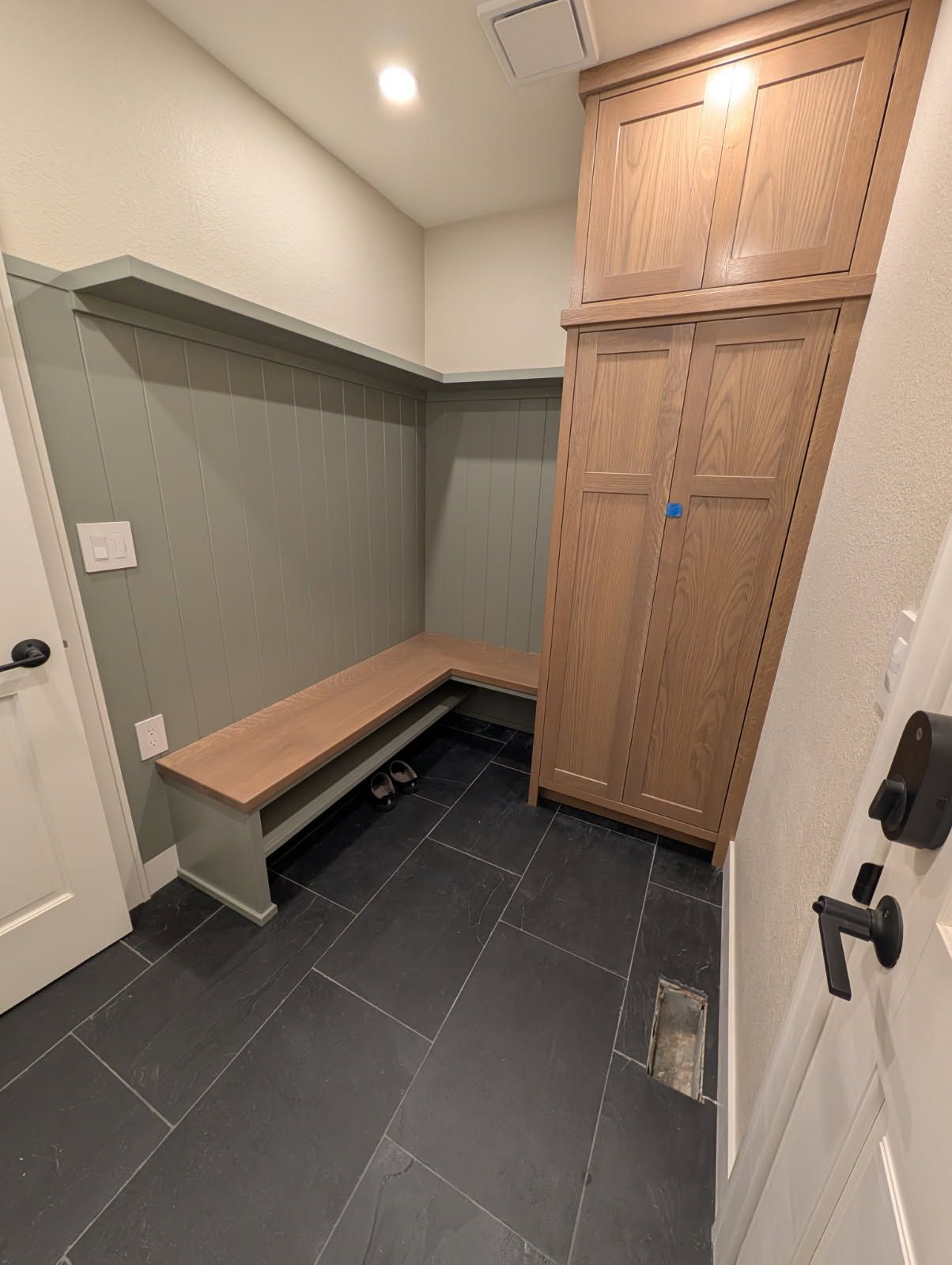 Narrow mudroom with gray tile, built-in wooden bench, tall storage cabinet, and white walls.